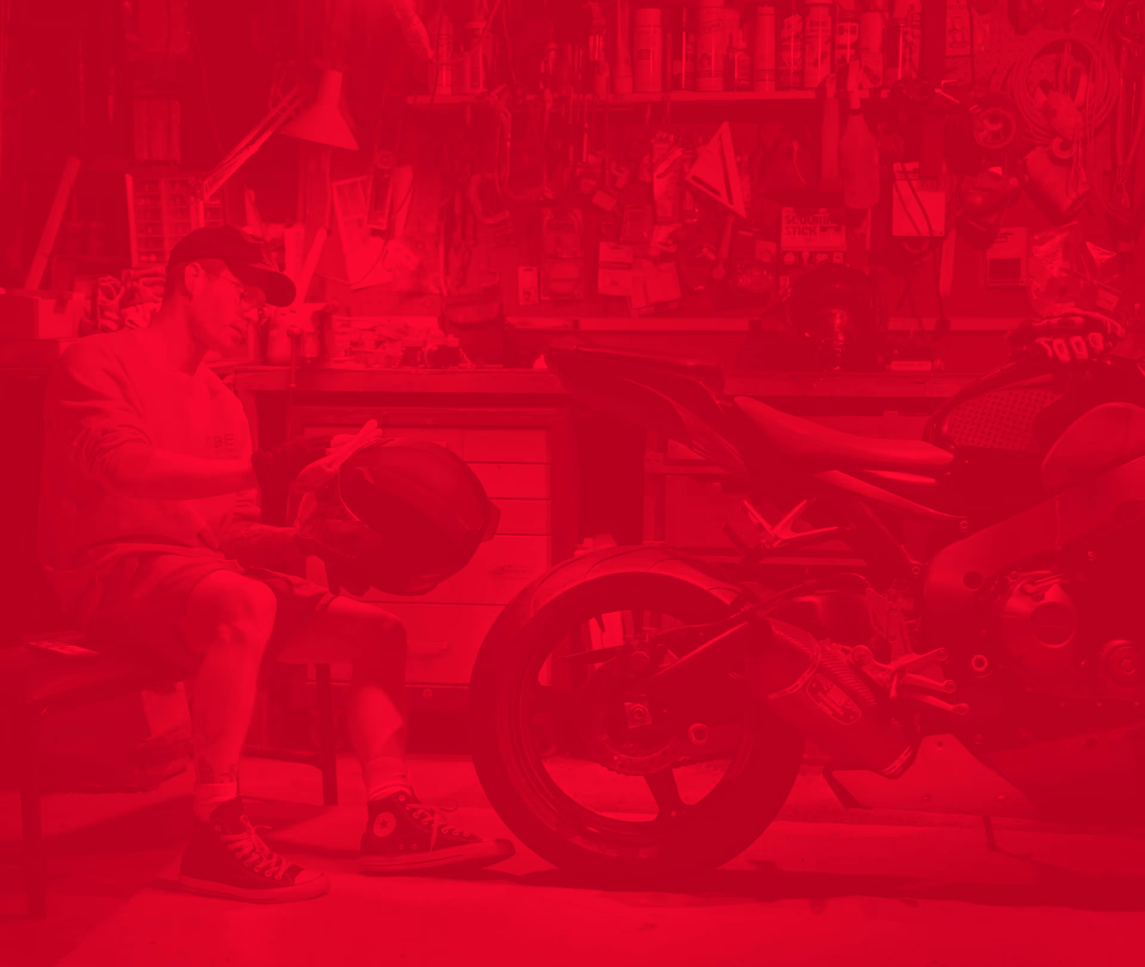 A man sits behind a motorcycle in a garage and polishes his helmet.